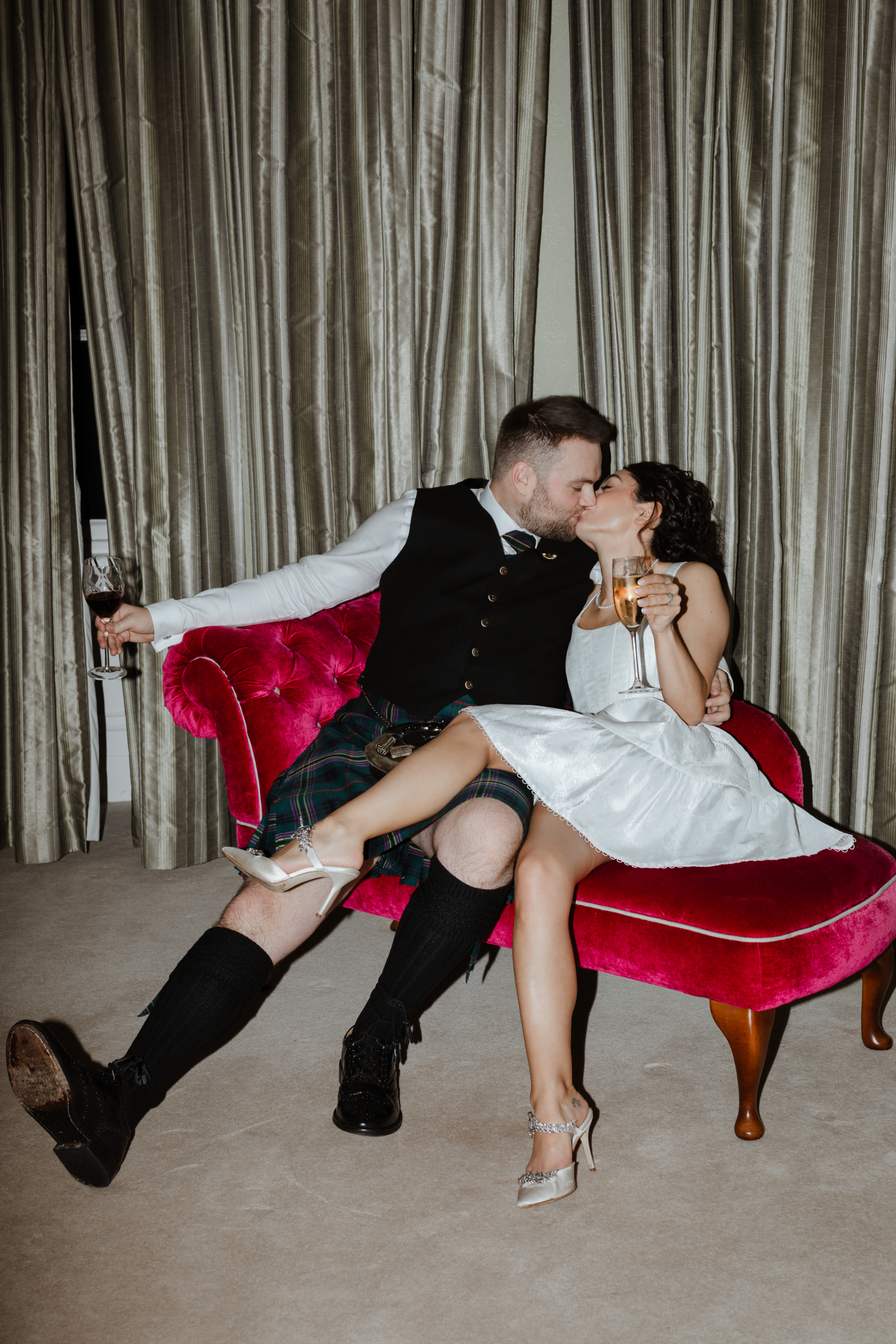 Submission Guidelines: How To Submit Real Weddings & Editorial Content to Love My Dress® 1 Bride in a short dress and groom in a kilt kissing on a red chaise longue. Caro Weiss Photography.